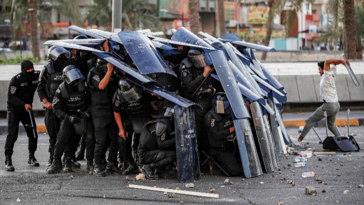 Irak-La policía antidisturbios iraquí se escuda en medio de los enfrentamientos, durante el cuarto aniversario de las protestas antigubernamentales iraquíes de 2019.