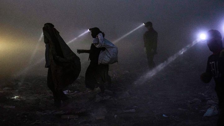 Irak-Personas equipadas con reflectores buscan material reciclable para revender en un vertedero en la ciudad de Basora, en el sur de Irak, a altas horas de la noche del 22 de junio