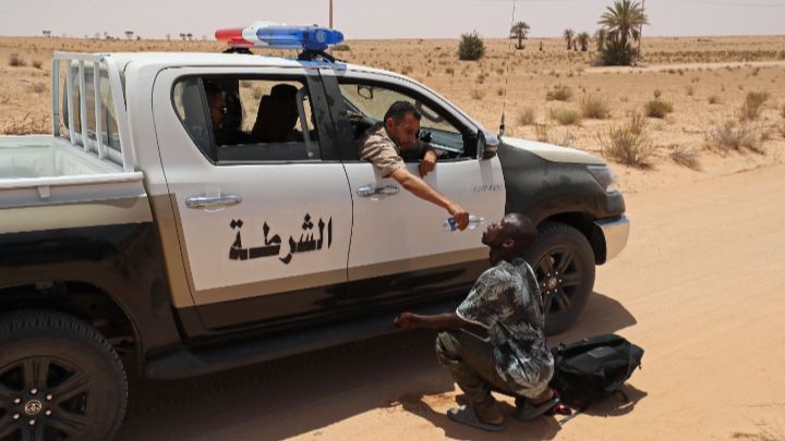 Libia-Un guardia fronterizo libio da agua a un migrante durante una operación de rescate en una zona deshabitada, el 16 de julio