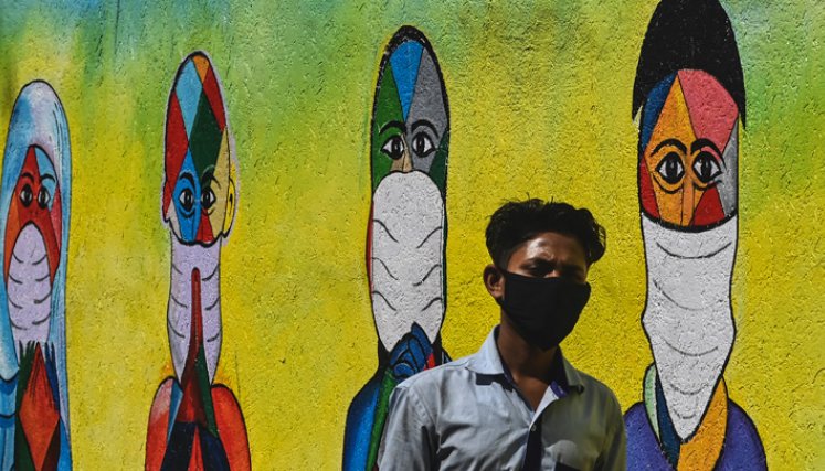 Un hombre pasa junto a un mural que muestra a personas de varias religiones agradeciendo a los guerreros del coronavirus de primera línea, en Mumbai. / Foto: AFP