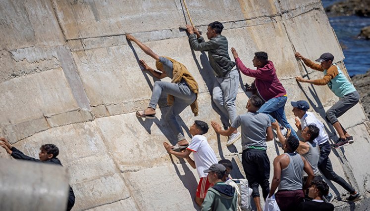 Migrantes escalan un malecón en la ciudad norteña de Fnideq después de intentar cruzar la frontera de Marruecos al enclave español de Ceuta.