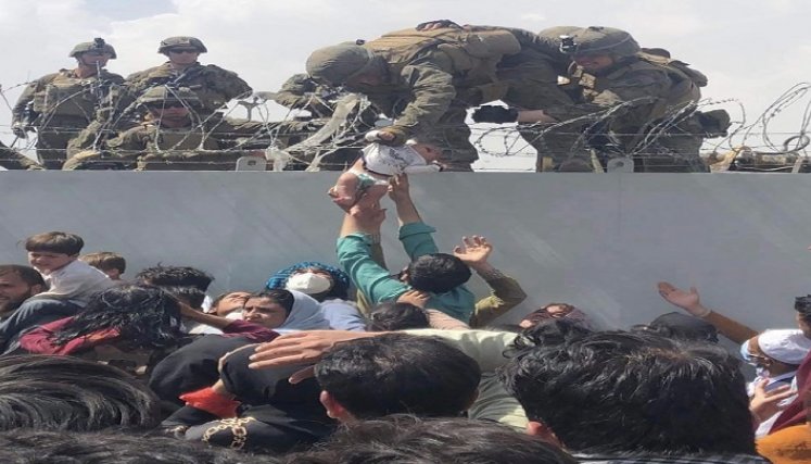 Un infante de marina estadounidense agarra a un bebé sobre una cerca de alambre de púas durante una evacuación en el aeropuerto de Kabul./ AFP