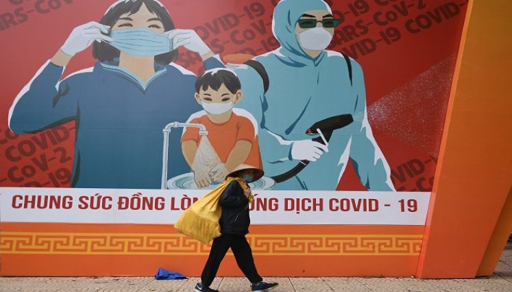una mujer pasa junto a una valla publicitaria con información sobre cómo prevenir la propagación del coronavirus Covid-19 en Hanoi./AFP