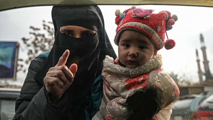 Una mujer carga a un niño mientras suplica a los viajeros en un automóvil en Kabul, el 26 de diciembre de 2021. / Foto:AFP